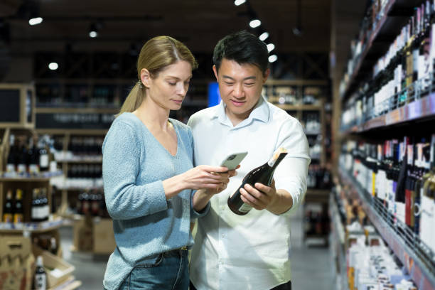 スーパーマーケットでアルコールワインを選ぶ多様な若い夫婦の男女の買い物客 - wine wine bottle drink alcohol ストックフォトと画像