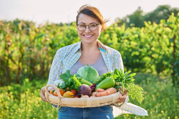 Portrait of smiling woman with basket of different fresh vegetables and herbs stock photo