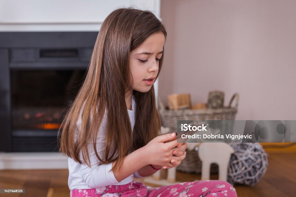 Tired girl starting her day with smart phone in hand Young tired girl waking up and holding smart phone right away 8-9 Years Stock Photo