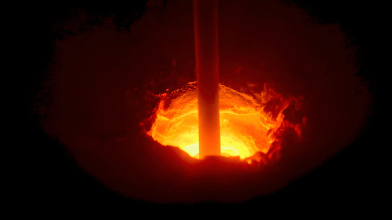 Close up of a hole in melting furnace with a rotating rod, metallurgical industry concept. Process of metal melting at the plant.