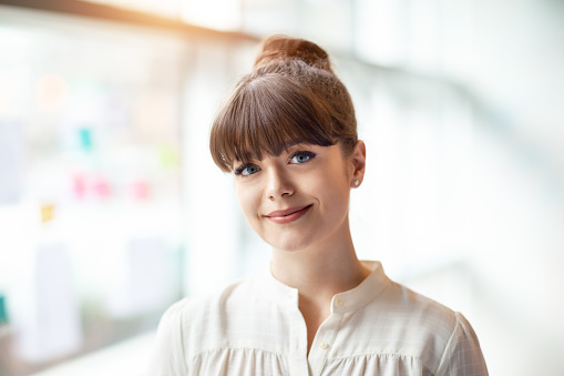 Portrait of young woman standing in modern office next to window