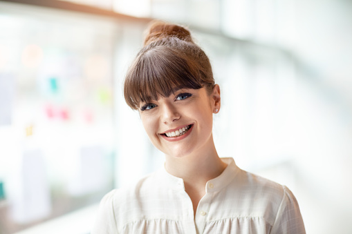 Portrait of young woman standing in modern office next to window