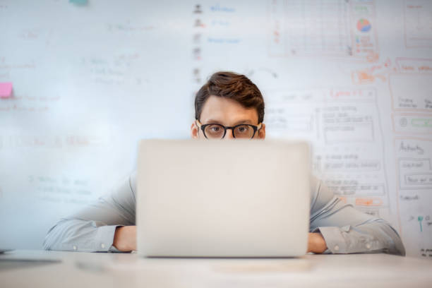 businessman looking at laptop screen while sitting at table in creative office - hiding humor occupation office imagens e fotografias de stock