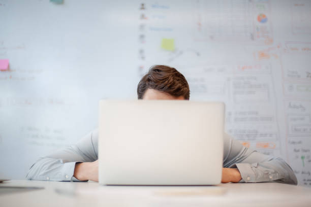 businessman looking at laptop screen while sitting at table in creative office - hiding humor occupation office imagens e fotografias de stock