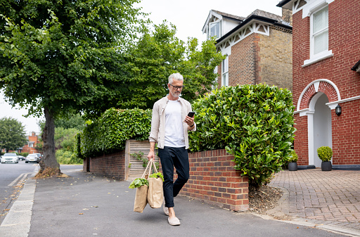 Caucasian man walking home with the groceries and using an app on his cell phone - lifestyle concepts