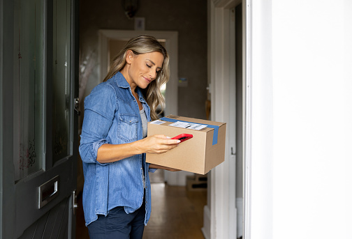 Happy woman receiving a package at home and getting a notification on her cell phone â domestic life concepts
