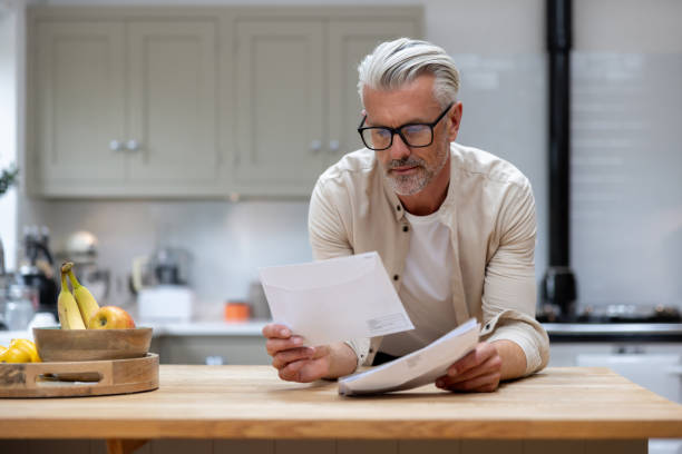 uomo a casa che legge una lettera nella sua posta - servizio postale foto e immagini stock