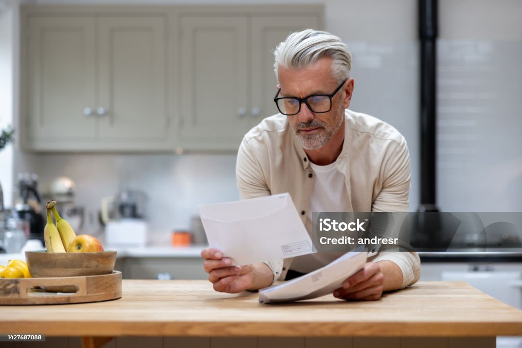 Man at home reading a letter in his mail Man at home reading a letter he got in his mail at the kitchen - lifestyle concepts Mail Stock Photo