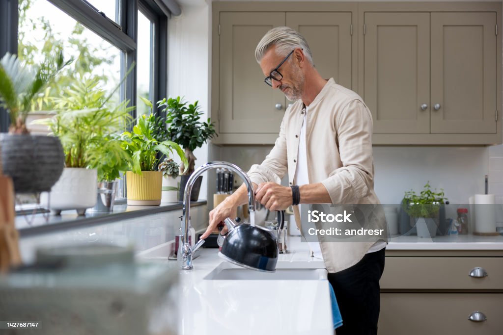 Man makign a cup of tea and putting the kettle on English man at home making a cup of tea and putting the kettle on - domestic life concepts Faucet Stock Photo