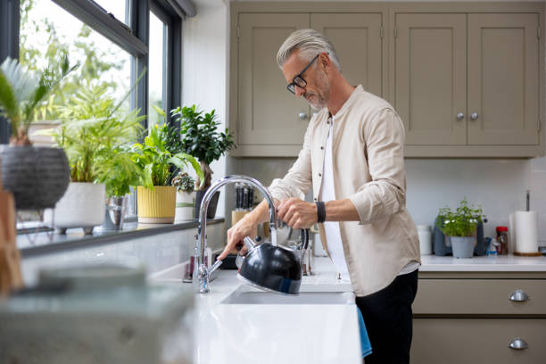 Man makign a cup of tea and putting the kettle on stock photo