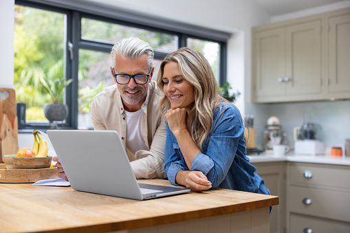 Happy Caucasian couple at home paying bills online using a laptop computer - home finances concepts