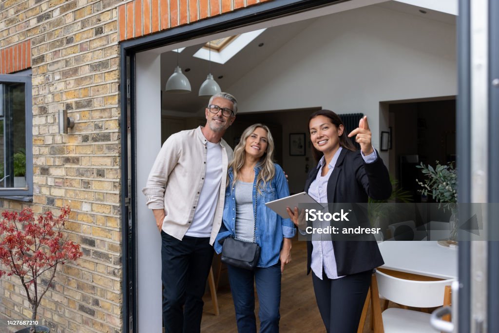Real estate agent showing a house for sale to a couple Real estate agent showing a house for sale to a couple and pointing outside - home ownership concepts Real Estate Agent Stock Photo