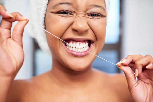Dental, cleaning and black woman flossing her teeth in a portrait in the bathroom for healthy oral maintenance. Lifestyle, wellness and young African girl doing a daily grooming and selfcare routine