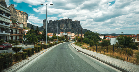 Wide angle shot from the open street in Greek Meteora, giant rock formations ahead, soft clouds in the background.