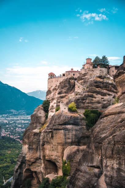 A vertical photo of an Orthodox monastery on top of a  boulder, popular with tourists. Side view of the building and the cliff.