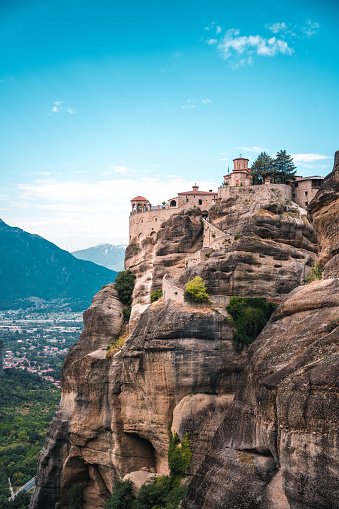 A vertical photo of an Orthodox monastery on top of a  boulder, popular with tourists. Side view of the building and the cliff.
