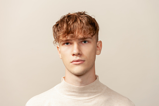 Close up studio portrait of a caucasian young man in a beige longsleeve on a beige background