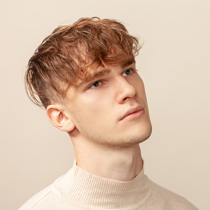 Close up studio portrait of a caucasian young man in a beige longsleeve on a beige background