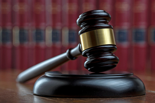 DARK JUDGE GAVEL ON THE TABLE IN THE COURTROOM AND LAW BOOKS IN THE BACKGROUND. CLOSE UP VIEW. FOCUS SELETED.