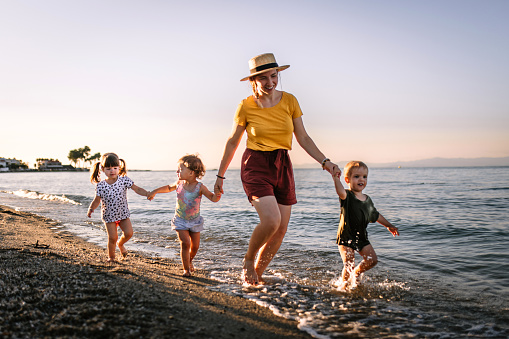 Mid adult woman at beach walk in sunset with three children. Running and having fun on the beach.