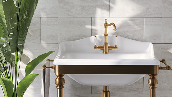 Diseño lujoso y clásico de tocador de baño con patas de latón, lavabo de cerámica rectangular blanco y planta de plátano con luz solar desde la ventana en la pared de mármol photo