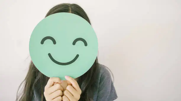preteen girl holding green happy smile face cover her face, mental health assessment, child positive wellness, world mental health day concept