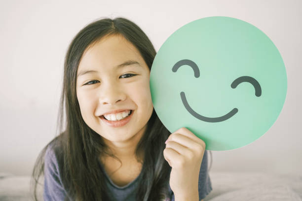 Mixed preteen girl holding green happy smile face paper cut, mental health assessment, child positive wellness, world mental health day concept Mixed preteen girl holding green happy smile face paper cut, mental health assessment, child positive wellness, world mental health day concept mental health ribbon stock pictures, royalty-free photos & images