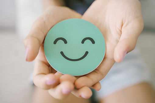 Hands holding green happy smile face paper cut, mental health assessment, child positive wellness, world mental health day concept