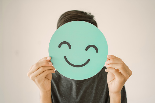 Adolescente feliz sosteniendo sonrisa emoji cara cubrir su rostro, concepto positivo de salud mental photo