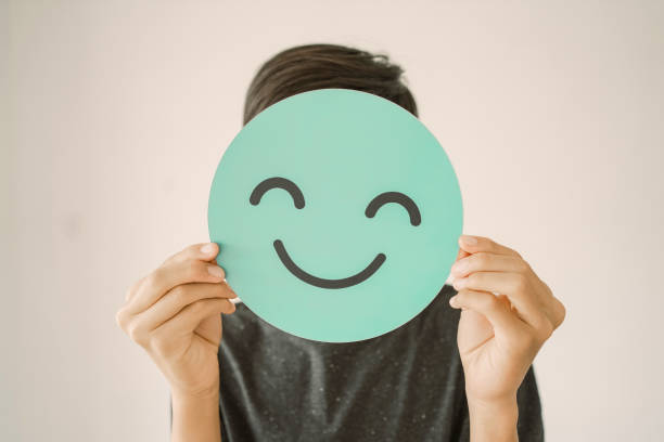 Happy  teen boy holding smile emoji face cover his face, positive mental health concept stock photo