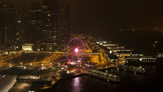 A nighttime view of the pier, river, ferris wheel and beautiful night city. Purple lighted ferris wheel near the river on night city background.