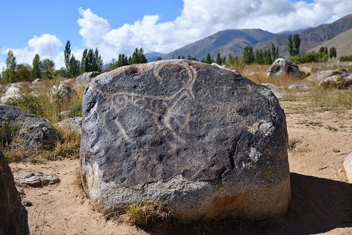 Mountain goat hunting scene on the stone against mountains. VII-III cc. BC. Cholpon Ata petroglyphs, Issyk Kul, Kyrgyzstan