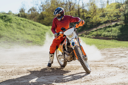 Rear view of man on dirt bike riding fast on off-road dirt track.