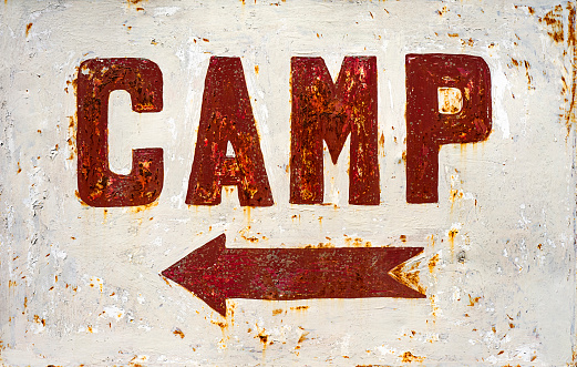 Rusty sign for camping near a road.