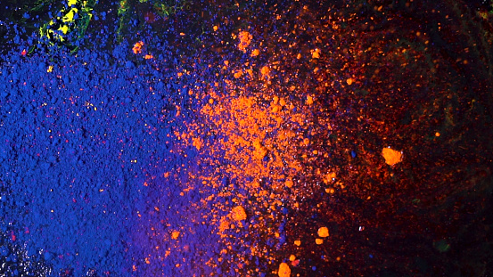 Top view of beautiful, bright colored powder falling and mixing. Dry orange and blue inks falling down on black background, art concept