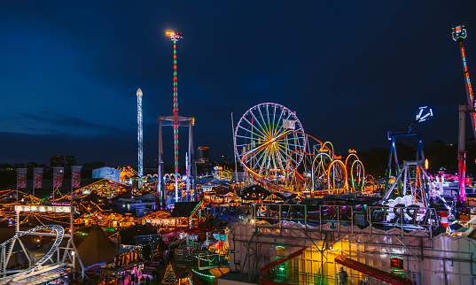 A roller coaster and drop ride lit in all colors as day turns into night at an amusement park.