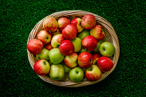 A bunch of green and red apples in a basket on the grass.