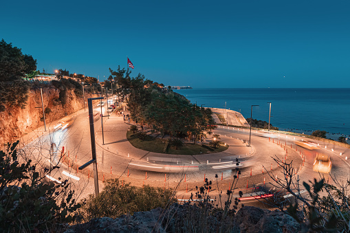 Cars and motorcycles climb the winding serpentine road to the observation deck with the Turkish flag and a wonderful view of the sea at night blue hour
