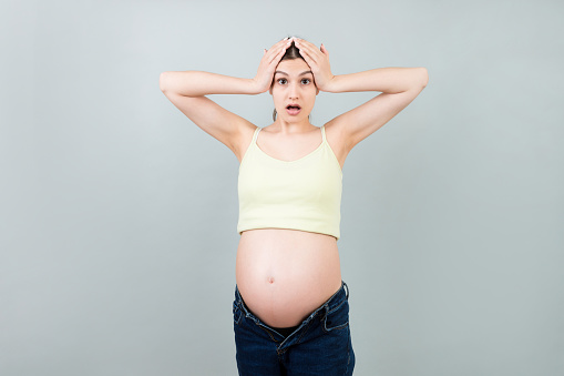 Picture of shocked or surprised pregnant lady standing over colored background. Looking at camera.