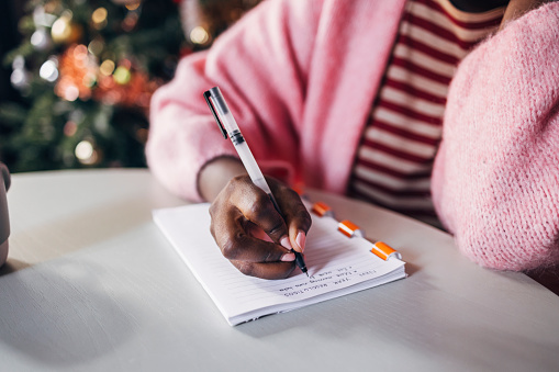 Close up shot of an anonymous Afro-Amercian woman writing plan for a New Year on a Christmas day.