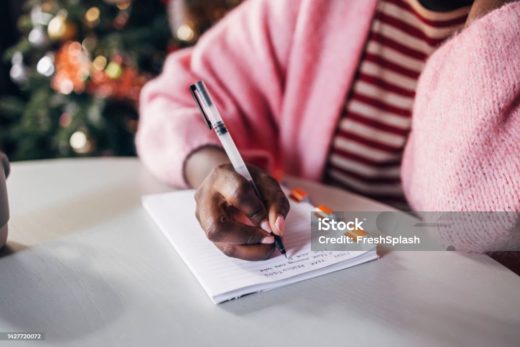 Woman Writing New Year's Resolutions Close up shot of an anonymous Afro-Amercian woman writing plan for a New Year on a Christmas day. New Year Resolution Stock Photo