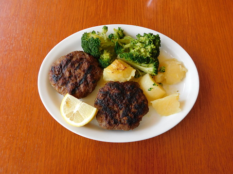 Grilled beef patties served with potatoes, lemon and broccoli