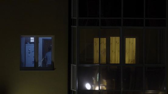 View on window of an apartment building outside at night. Wall with iIluminated windows. Detail of soviet era block apartment building.