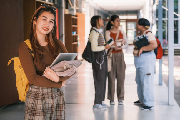 istock Portrait of Asian college women students holding laptop computer and backpack while her friends standing in background at university campus 1427747921