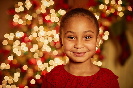 Close up portrait of cute black girl smiling at camera on Christmas eve, copy space