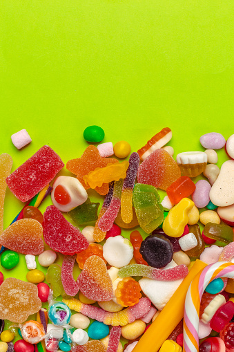 Top view of an assortment of multicolored candies, lollipops and jelly beans background. All the candies are at the borders of the image making a frame shape and leaving a useful copy space at the center of the image on a withe background.  Studio shot taken with Canon EOS 6D Mark II and Canon EF 24-105 mm f/4L