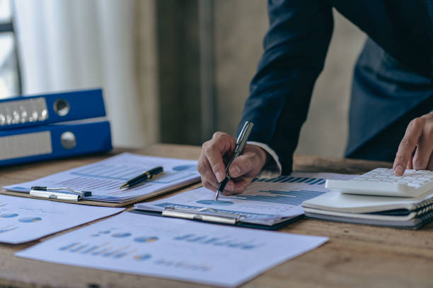 istock Businessman holding pen pointing to graph while analyzing financial paper graph and on desk at office 1427797223