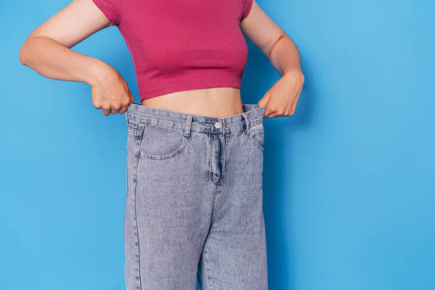 Girl in blue jeans that is several sizes larger in front of a blue background stock photo