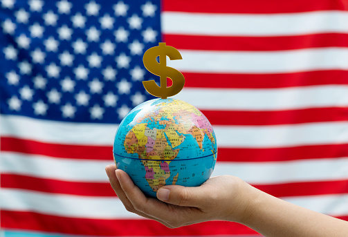 World globe and dollar sign in front of American flag.
