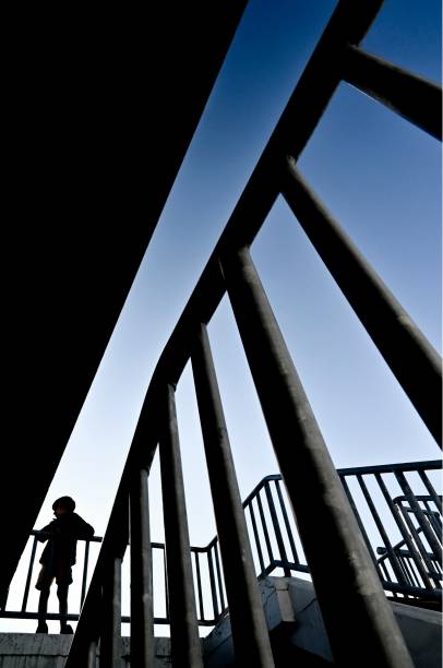 Boy in silhouette looks into distance among dramatic arrangement of stair handrails
